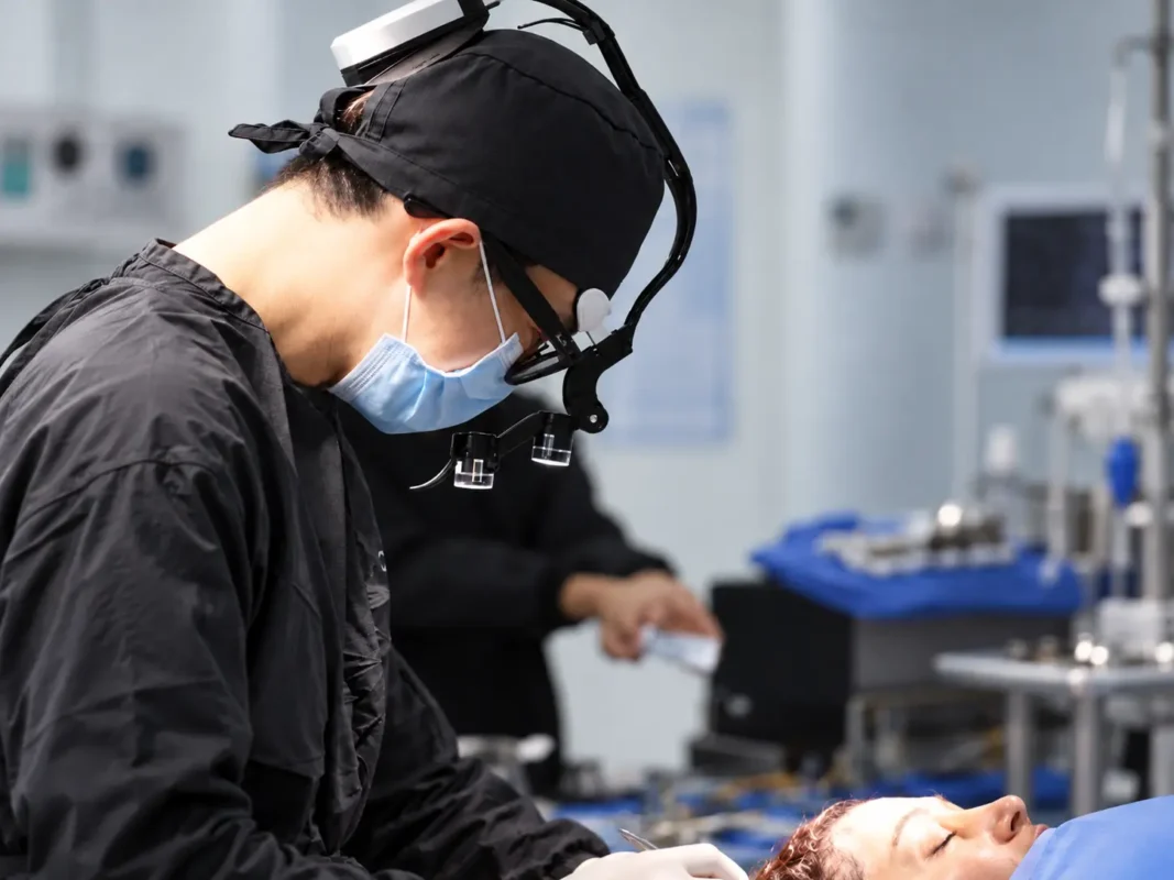 Plastic surgeon performing forehead reduction surgery (hairline lowering) with surgical loupes in an operating room in Medellín, Colombia